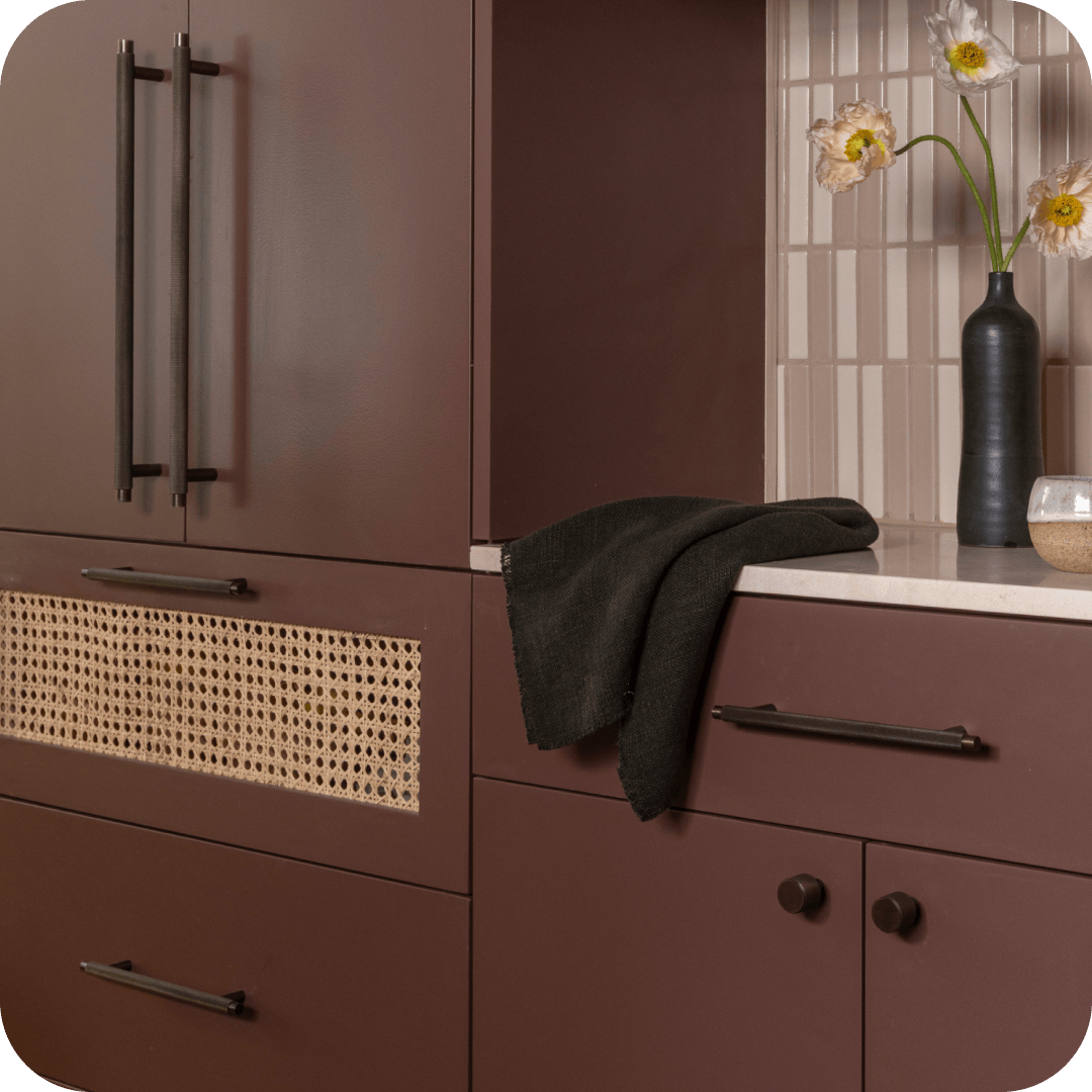 Oxblood kitchen cabinetry fitted with knurled bronze T-bar pulls and round cabinet knobs, beside a cane-panelled drawer front